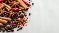 Aromatic cooking spices scattered on white background including cinnamon sticks, star anise, peppercorns and chili flakes for culinary seasoning.