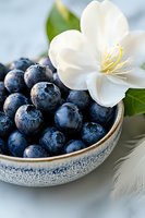 Fresh ripe blueberries in ceramic bowl with water drops and white jasmine flower, close up view on light background. For food blogs and healthy eating.