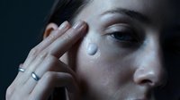 Young woman applying facial cream or moisturizer to her face with gentle hand movements for daily skincare routine and beauty treatment.