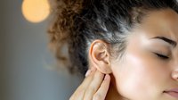 Young mixed race woman with curly hair touching ear in pain, experiencing discomfort or earache against blurred background with bokeh lights.