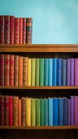 Rainbow-colored books arranged in gradient order on wooden shelves against a turquoise wall, creating a vibrant library display.