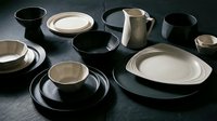 Modern ceramic dinnerware set with black and beige plates, bowls, cups and pitcher arranged on dark surface for contemporary kitchen and dining decor.