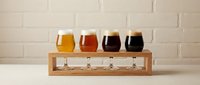 Craft beer tasting flight with four glasses of different colored beers in wooden holder for brewery sampling and beverage comparison.