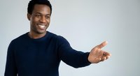 Young African American man in navy sweater pointing and smiling on white background, isolated for design use in presentations and marketing materials.
