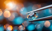 Brilliant diamond held by tweezers against blurred bokeh background with orange and blue lights, showcasing luxury jewelry craftsmanship.