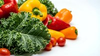 Fresh organic vegetables including kale, bell peppers and cherry tomatoes arranged on white background for healthy cooking and nutrition concepts.