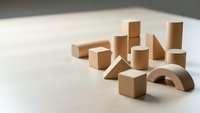 Wooden building blocks set with geometric shapes including cubes, cylinders and triangles arranged on neutral surface for educational play and development.