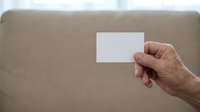 Mature adult hand holding blank white business card against neutral beige background for branding and corporate identity mockup purposes.
