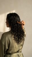 Young woman with wet curly hair combing locks in bathroom wearing green robe. Hair care routine, styling wet curls, personal grooming and beauty concept.