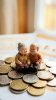 Elderly couple figurines sitting on pile of coins representing retirement savings, pension planning and financial security for senior years.