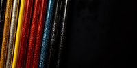 Colorful metallic glitter lines on black background create modern abstract composition with gold, yellow, red and blue stripes in minimalist style.