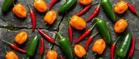 Assorted fresh hot chili peppers on dark stone surface, flat lay. Jalapeno, habanero, and cayenne varieties for cooking and spicy food concepts.