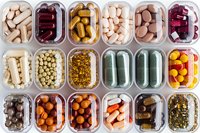 Various dietary supplements and vitamins in plastic containers viewed from above, showing colorful capsules, pills, and tablets arranged in organized compartments.
