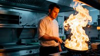 Professional male chef cooking with dramatic flames in commercial kitchen, culinary expertise and restaurant cooking skills in action.