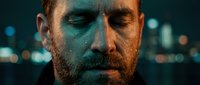 Young adult male with reddish-brown beard and fair complexion, eyes closed in contemplation against blurred city lights. Suitable for mental health, stress, depression, and wellness concepts.