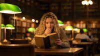 Young blonde woman reading book in cozy library with warm lighting and green banker lamps creating studious atmosphere for education and learning.