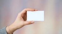 Hand holding blank white card against blurred background, suitable for business branding, marketing mockups, and corporate identity presentations.