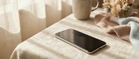 Modern smartphone on linen tablecloth with coffee cup and dried flowers in warm natural sunlight creating cozy morning atmosphere for lifestyle content.