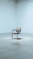 Modern office chair with beige upholstery and metal frame positioned in minimalist interior space with white walls and concrete flooring for contemporary workspace design.