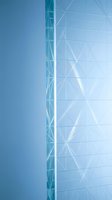 Modern glass facade with geometric triangular pattern and metal framework against clear blue sky, suitable for corporate and architectural design projects.