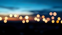 Dreamy defocused city lights create golden bokeh effect against dramatic dusk sky with deep blue and orange gradient, abstract urban nightscape background.