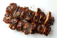 Grilled pork ribs sliced into portions, glazed with sweet and savory barbecue sauce, garnished with fresh herbs and black pepper on white background.