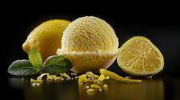 Fresh lemon ice cream scoops with citrus fruit, zest and mint leaves on dark background, dramatic lighting creates appetizing dessert composition.