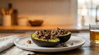 Halved avocado topped with seasoned ground meat served on white plate in modern kitchen setting, suitable for healthy meal planning and food photography.