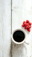 Cup of black coffee with fresh raspberries on rustic white wooden surface, overhead view. Suitable for food blogs, café menus, breakfast content, and lifestyle marketing materials.