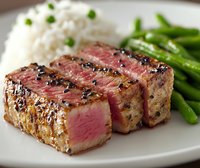 Juicy grilled pepper steak sliced to show medium-rare center, served with white rice and steamed green beans on white plate, close up food photography.