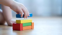 Child hand stacking colorful wooden blocks on floor developing fine motor skills and creativity through educational play activity.