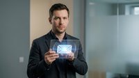 Caucasian male professional in dark blazer holding tablet displaying envelope icon in modern office setting, representing digital communication and business technology.