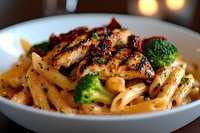 Grilled chicken penne pasta with broccoli florets in creamy sauce, garnished with black pepper and herbs, served in white ceramic bowl.