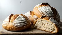 Artisan sourdough bread loaves with distinctive scoring patterns on wooden cutting board, showcasing golden crust and airy crumb texture for bakery marketing.