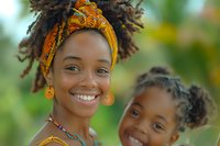 African woman and child smiling outdoors, wearing bright yellow traditional headwrap and jewelry against natural green background, expressing joy and family connection.