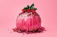 Pink glazed holiday dessert decorated with holly leaves and berries, dripping icing, and sparkly red sugar sprinkles on pink background.
