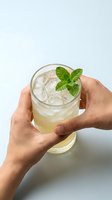 Hands holding refreshing mint cocktail with ice cubes on white background for beverage and drink concepts.