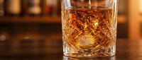 Golden whiskey in crystal cut glass with ice cube on wooden bar counter. Luxury spirits and premium alcohol beverage for cocktail preparation and tasting.
