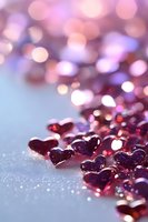 Small pink and purple heart-shaped decorative elements on glittery surface with soft bokeh background in romantic pastel colors, creating dreamy Valentine's Day atmosphere.