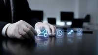 Businessman hand touching digital email icon with business analytics symbols on modern office desk for corporate communication and data management.