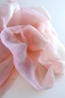 Soft pink delicate chiffon fabric with gentle folds and flowing curves creates ethereal abstract composition against white background. Suitable for fashion and wedding designs.