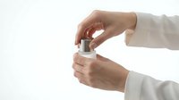 Woman's hands in white long-sleeved shirt opening cosmetic jar with cream or skincare product on white background for beauty and wellness design use.