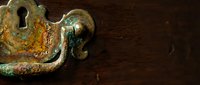 Vintage brass keyhole escutcheon with patina and rust on dark wooden surface showing antique hardware detail and aged metal texture for restoration projects.