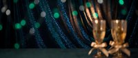 Elegant champagne glasses with sparkling bokeh lights and glittery fabric creating luxurious celebration atmosphere for New Year or special events.