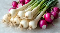 Fresh spring onions with white bulbs and green stems alongside bright pink radishes on light background, raw organic vegetables for healthy cooking.