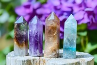 Crystal points collection featuring fluorite, amethyst, citrine and aquamarine minerals displayed on wooden surface against purple floral background in natural light.