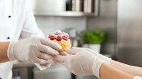 Professional chef in white gloves presenting gourmet dessert in modern kitchen. Culinary artistry and fine dining presentation for restaurant menu.