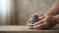 Hands gently holding stack of smooth zen stones on wooden surface creating peaceful meditation and mindfulness concept for wellness and balance.