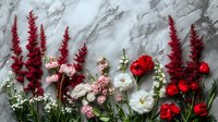 Romantic floral arrangement with red astilbe, pink and white ranunculus, and red roses against gray marble background for wedding decor and greeting cards.
