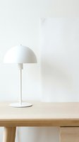 Minimalist white dome table lamp with metal stem on wooden desk against neutral background, suitable for interior design and home decor projects.